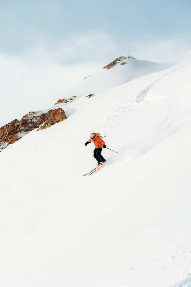 Person skiing down a mountain peak with a view of the summit in the background.
